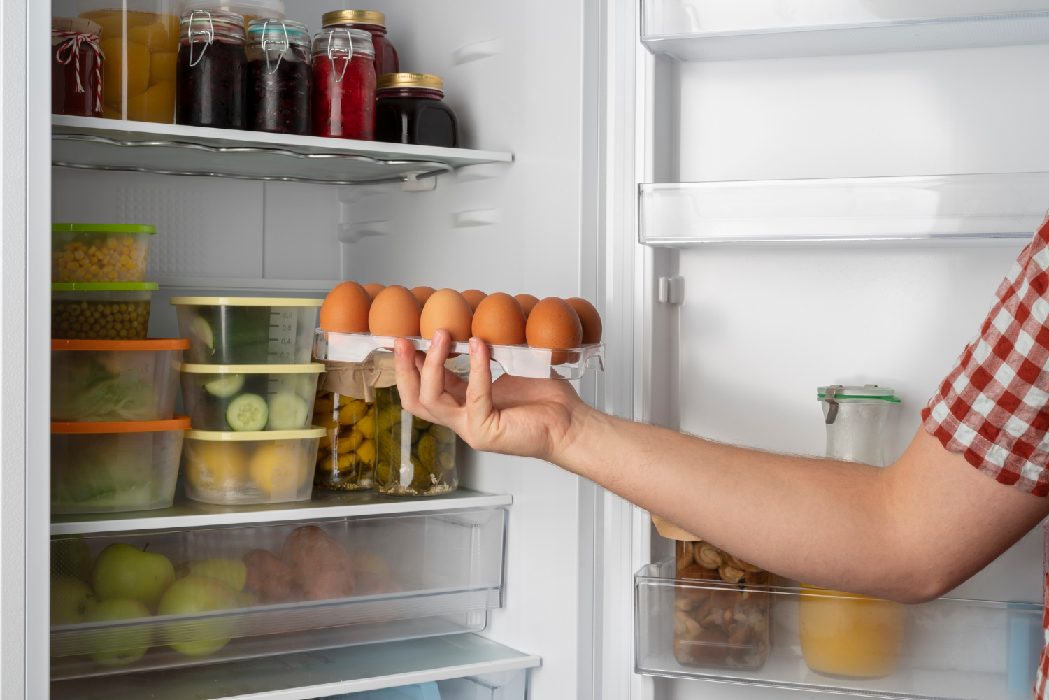 2149185613 A person holds a carton of eggs in front of an open refrigerator filled with food and containers.