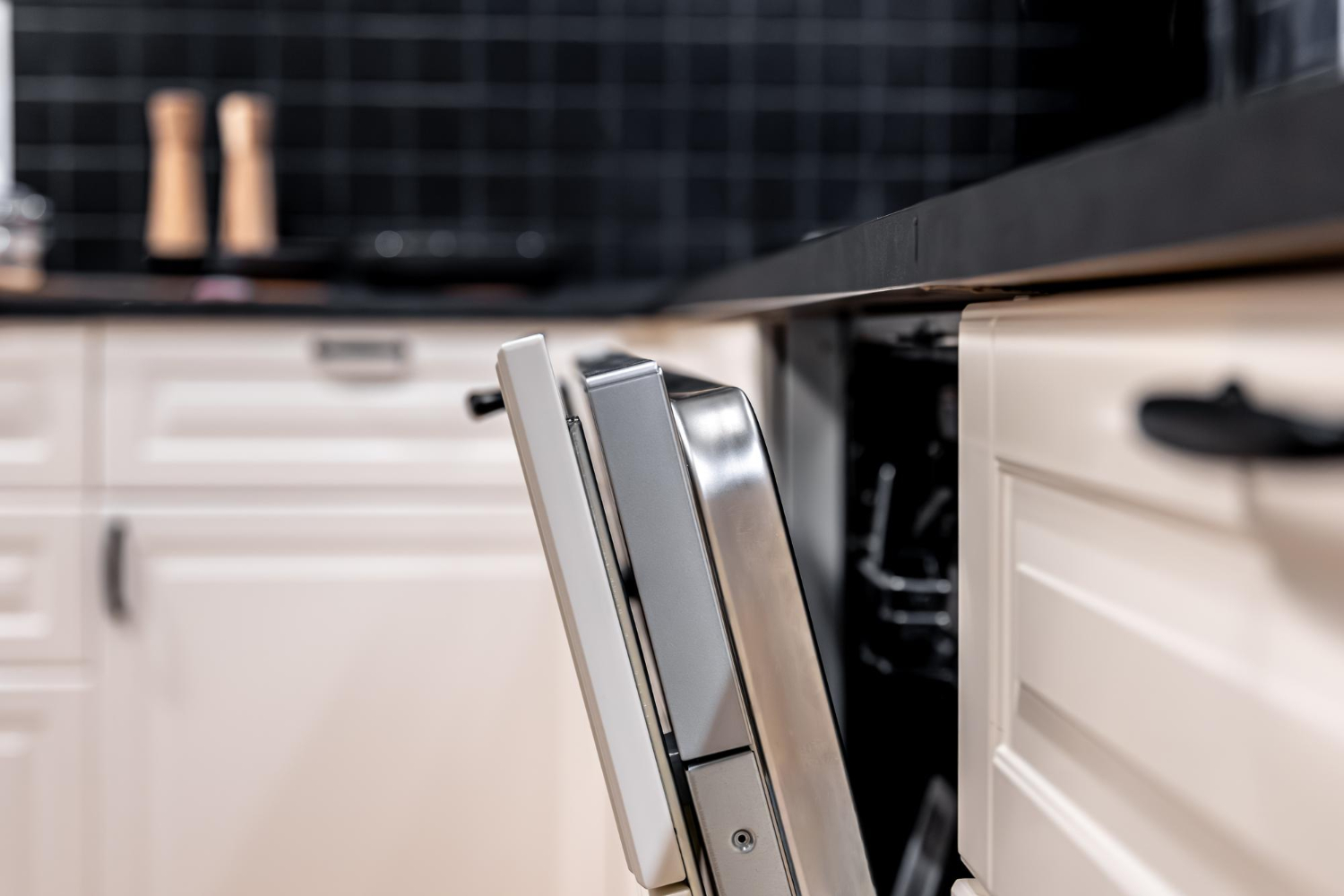 71056 A partially open dishwasher in a modern kitchen with white cabinets and a black tiled backsplash.