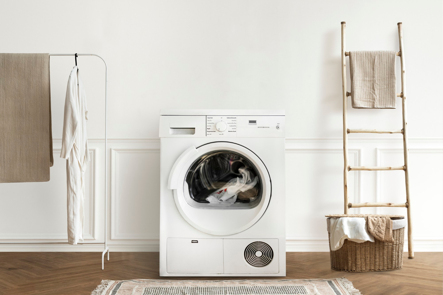 Front-loading washing machine in a minimal laundry room with neutral towels and wooden ladder décor.